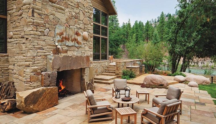 Wooden armchairs and tables in the rustic garden with a large stone fireplace